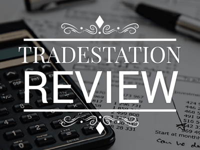 This image features the prominent white text "TRADESTATION REVIEW" centered on a black background, framed by decorative white flourishes and horizontal lines above and below, with a small diamond shape at the very top and bottom. The background of the image, partially obscured by the text, shows financial documents and a calculator, subtly hinting at the mathematical and analytical aspects of investing discussed in the accompanying article. The calculator, with visible numerical buttons and a small display, represents the quantitative nature of trading, while the papers likely contain figures and data relevant to asset allocation, stock trades, and brokerage fees. This visual reinforces the article's focus on TradeStation as an investing software for active traders, emphasizing the data-driven approach needed to gain an edge in the market.