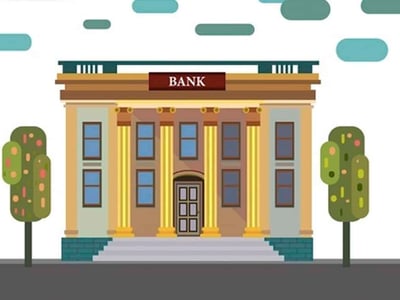 An illustrative image of a traditional, neoclassical bank building with the word "BANK" prominently displayed above its entrance, flanked by tall columns. The building features multiple windows with dark panes and a set of steps leading up to the main door, all rendered in a flat, cartoonish style. Two stylized green trees with rounded leaves stand on either side of the bank, against a muted background with hints of teal shapes suggesting clouds or abstract elements. In the bottom left corner, the white text "THE COLLEGE INVESTOR" is visible, indicating the source of this review. This visual represents the banking services and products, such as high-yield savings accounts and business checking, offered by institutions like Customers Bank, discussed in the accompanying article.