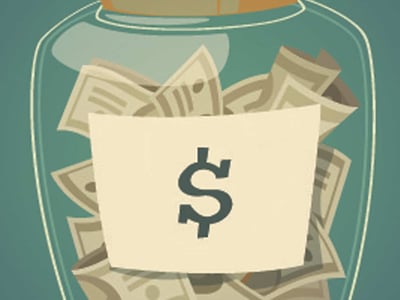A clear glass jar, half-full with an assortment of paper money and a few gold coins, sits prominently against a teal background, symbolizing saving and business income. A beige label with a bold black dollar sign is affixed to the front of the jar, emphasizing the financial aspect. The jar has a light brown, flat lid. In the bottom left corner, the white text "THE COLLEGE INVESTOR" is visible, indicating the source of the article content. This image visually represents the concept of managing business and personal income, a crucial step for entrepreneurs separating their finances with a small business checking account like the one offered by Novo, as discussed in the review of top business checking accounts.