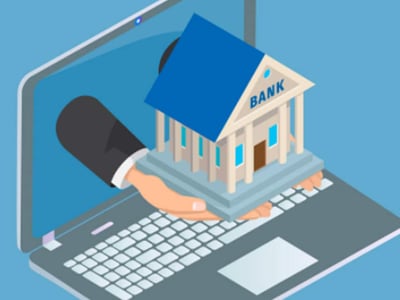 An isometric digital illustration depicts a human hand, emerging from the screen of a silver laptop, presenting a miniature bank building. The hand has light skin and is clad in a dark suit sleeve with a white cuff, holding the small, classic-style bank with a blue roof, white columns, and the word "BANK" clearly visible above the entrance. The laptop itself is open with its keyboard and screen visible against a solid blue background. This visual metaphor effectively represents the discussion in the article about Truist Bank, formed from the merger of BB&T and SunTrust, emphasizing the accessibility of banking services, including checking and savings accounts, through digital platforms, even as the new financial company expands its physical branches and ATM access for approximately 10 million households.