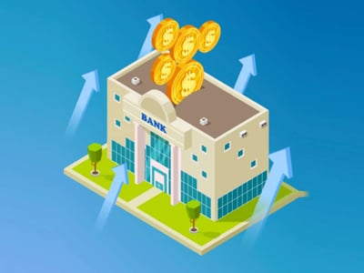An isometric illustration on a blue background depicts a stylized, light brown bank building with "BANK" written above its entrance, featuring classical columns and large windows. Above the bank, several gold coins are stacked, with five coins visible, suggesting financial growth and high returns. Four light blue arrows emanate from around the bank's foundation and point upwards, further emphasizing the concept of increasing value or high yield, directly relating to the article's focus on high-interest checking accounts. The foreground prominently displays the text "THE COLLEGE INVESTOR," identifying the source of the financial advice. This image visually represents the core concept of a bank generating high interest on checking accounts, connecting directly to the article's discussion of the best high-yield checking account options available.