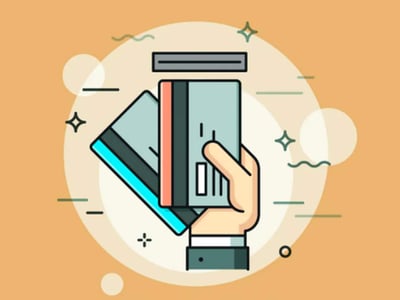 A graphic illustration shows a human hand holding two debit cards in front of a rectangular card reader, symbolizing a transaction with a Greenlight debit card and app designed for kids and teens. The hand and cards are centered within a large, translucent white circle, which is overlaid on a warm, sandy-orange background. Various decorative elements like small stars, wavy lines, and additional translucent circles float around the central image, creating a sense of digital activity and financial movement. The bottom left corner features the text "THE COLLEGE INVESTOR" in a bold, white sans-serif font, indicating the source of this review of Greenlight, a popular tool for parents to teach their children about managing money in the modern economy.