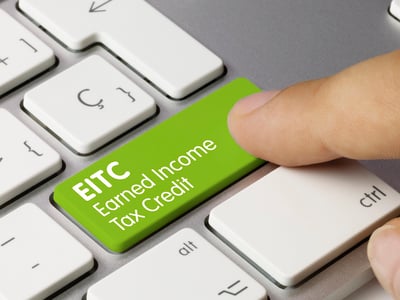 Close-up of a finger pressing a computer keyboard key next to a bright green button labeled "EITC Earned Income Tax Credit." This illustrates that eligible taxpayers must actively claim the benefit on their return, as the IRS does not apply it automatically. Source: The College Investor