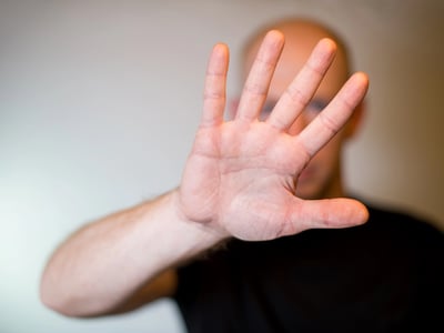 A person with a blurred face and bald head extends their right hand towards the viewer, palm open and fingers spread, in a clear "stop" or "hold" gesture. This image effectively symbolizes the Department of Education's decision to allow existing federal student loan borrowers to retain their current fixed repayment plans—Standard, Extended, and Graduated—after July 1, 2026. The hand gesture visually represents the pause or exemption for these borrowers from the new "tiered standard" repayment plan being introduced by the "One Big, Beautiful Bill Act" for future student loan recipients.