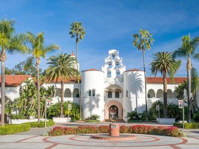 Sunny view of San Diego State University campus featuring a white bell tower and palm trees. This illustrates California institutions facing legal challenges over student aid and the financial pressures cited in Moody's 2026 outlook for higher education. Source: The College Investor