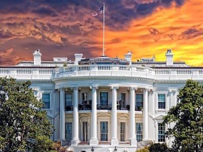 The White House stands under a dramatic sky filled with vivid orange and purple sunset clouds, symbolizing the dawn of the new Trump Accounts program. This image accompanies the guide on claiming the $1,000 "Baby Bonus" for children born 2025–2028, a major federal savings initiative launching with a philanthropic boost from the Dell Foundation. Source: The College Investor