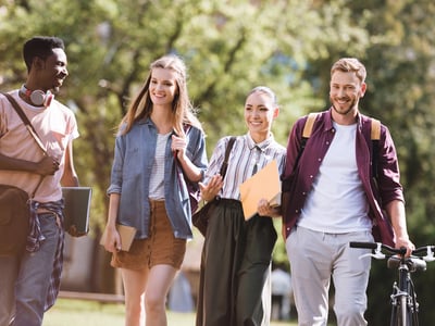 Diverse group of smiling college students walking together on a sunny campus path, carrying backpacks and books. This image illustrates the value of perseverance, specifically encouraging sophomores to re-file the FAFSA for potential financial aid opportunities they may have missed as freshmen. Source: The College Investor