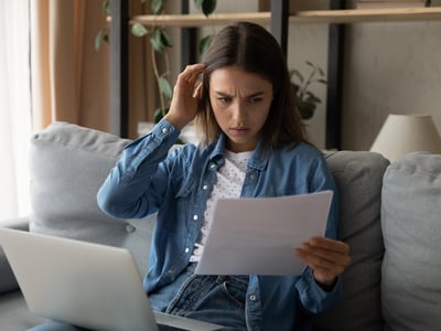 A photo of a woman looking at her student loan statement and laptop and wondering why it says in default but that's not accurate. This ties into the article about incorrect default notices on StudentAid.gov
