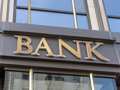 Large gold "BANK" sign on a corporate building facade. This symbolizes private lenders facing underwriting challenges to replace federal Grad PLUS loans for high-cost graduate and professional programs. Source: The College Investor