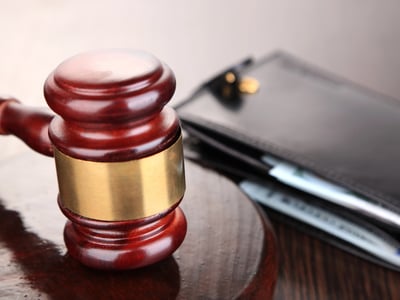 Wooden gavel resting next to a black wallet filled with cash. This symbolizes the legal resumption of wage garnishment for defaulted federal student loans starting in early 2026. Source: The College Investor