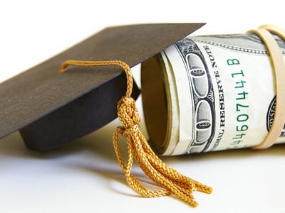 Close-up of a black graduation cap with a gold tassel resting next to a thick roll of U.S. dollar bills secured by a rubber band. This image symbolizes the significant financial shifts facing students and families in 2026, including the end of Grad PLUS loans, new caps on Parent PLUS borrowing, and the transition to the Repayment Assistance Plan (RAP). Source: The College Investor