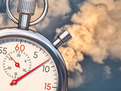 Close-up of a silver stopwatch held against a backdrop of stormy clouds and blue sky. The stopwatch hands are in sharp focus, symbolizing the urgency of the upcoming 2028 sunset date for the PAYE and ICR student loan repayment plans, while the turbulent sky represents the uncertain transition period borrowers face.