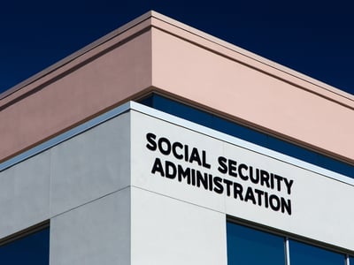 Exterior view of the Social Security Administration building with bold black signage on the facade. This image represents the structural financial challenges facing the program, including a projected trust fund depletion by 2033, which could result in benefit cuts if Congress does not enact reforms such as adjusting payroll taxes or retirement age. Source: The College Investor