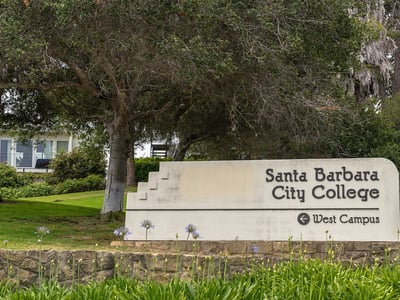 Santa Barbara City College facilities. Closeup, White stone with black name sign set in green garden with tree at entrance to the campus.