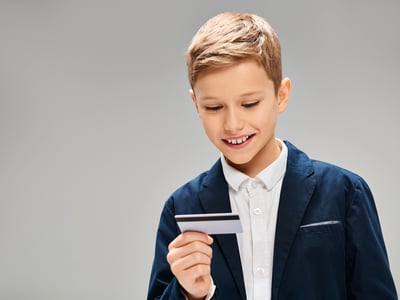 A picture of a schoolage boy holding a credit card, representing financial literacy in America. Source: The College Investor