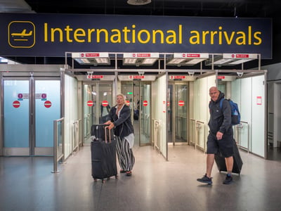Male and female passengers with luggage walk through International Arrivals at airport, reflecting the change in international student enrollment at US colleges.