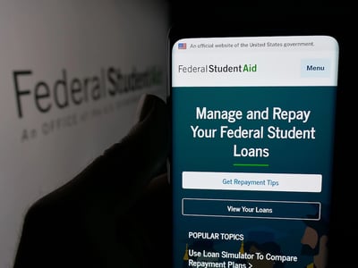 Person holding smartphone with web page of education office Federal Student Aid (FSA) on screen in front of logo. Focus on center of phone display.