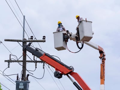 electrician works on bucket car to maintain high voltage transmission lines.