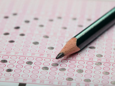 School Students hands taking SAT exam, writing examination holding pencil on optical form of standardized test with answers sheet doing final exam in classroom.