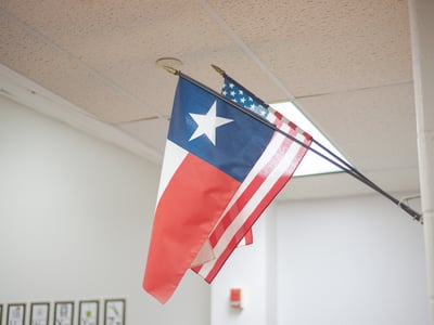 School in Dallas Fort Worth highlights Texas flag angled beside national banner on white wall.
