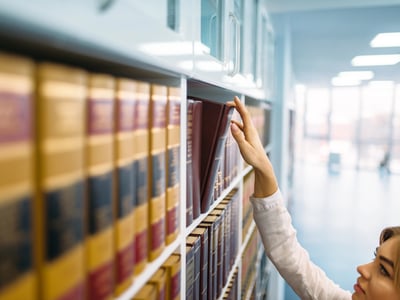 Female librarian looking book at the shelf in law library.