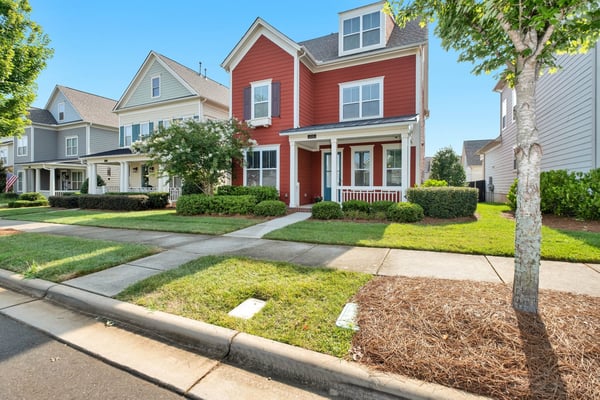 Photo by Zac Gudakov on Unsplash This image showcases a charming two-story red house with white trim and a welcoming front porch, situated in a well-maintained suburban neighborhood. Lush green lawns, manicured bushes, and mature trees line the sidewalk and street, creating a pleasant residential atmosphere. Other similar homes, some in lighter shades of gray and beige, are visible further down the street under a clear blue sky. This visual context is highly relevant to an article discussing reverse mortgages, home equity loans, and HELOCs, as it depicts the type of residential property where homeowners, particularly those 62 or older, might consider leveraging their home equity to supplement their monthly retirement income. The house represents the valuable asset that serves as collateral for a reverse mortgage, highlighting the importance of property ownership for seniors seeking financial flexibility.