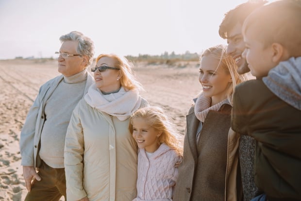Multigenerational Family A multi-generational family of six, including grandparents, parents, and two young children, stands together on a sunny beach, smiling and looking out toward the horizon. They are dressed in warm, neutral-toned fall or winter coats and scarves. This image visually represents the concept of family support and interconnectedness, reflecting the article's focus on how rising student debt and housing costs are increasingly causing young adults to rely on their parents for financial help, impacting multiple generations' financial futures. Source: The College Investor