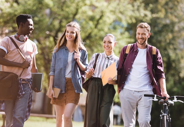 Diverse group of smiling college students walking together on a sunny campus path, carrying backpacks and books. This image illustrates the value of perseverance, specifically encouraging sophomores to re-file the FAFSA for potential financial aid opportunities they may have missed as freshmen. Source: The College Investor