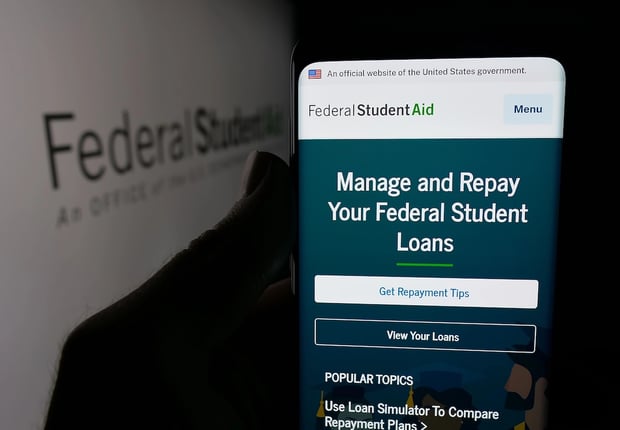 Person holding smartphone with web page of education office Federal Student Aid (FSA) on screen in front of logo. Focus on center of phone display.