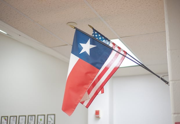 School in Dallas Fort Worth highlights Texas flag angled beside national banner on white wall.