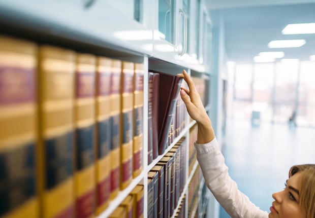 Female librarian looking book at the shelf in law library.