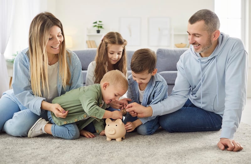 Happy family with kids putting money coin into piggy bank sitting at home together. Best custodial investment accounts | Source: The College Investor