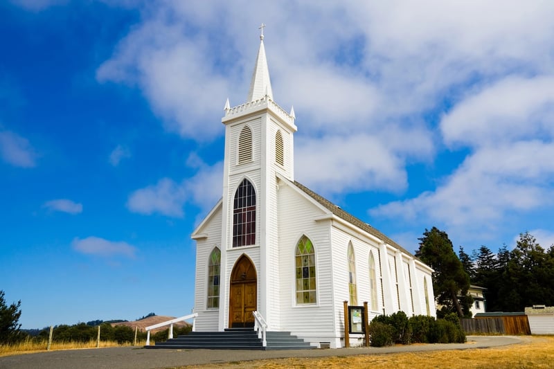 Little White Church Traditional white wooden church with a tall steeple and arched stained-glass windows, standing against a bright blue sky with white clouds. This image represents the analysis of educational attainment among U.S. religious groups, specifically highlighting the diverse range of college completion rates within Christian denominations, from Episcopalians to evangelicals. Source: The College Investor