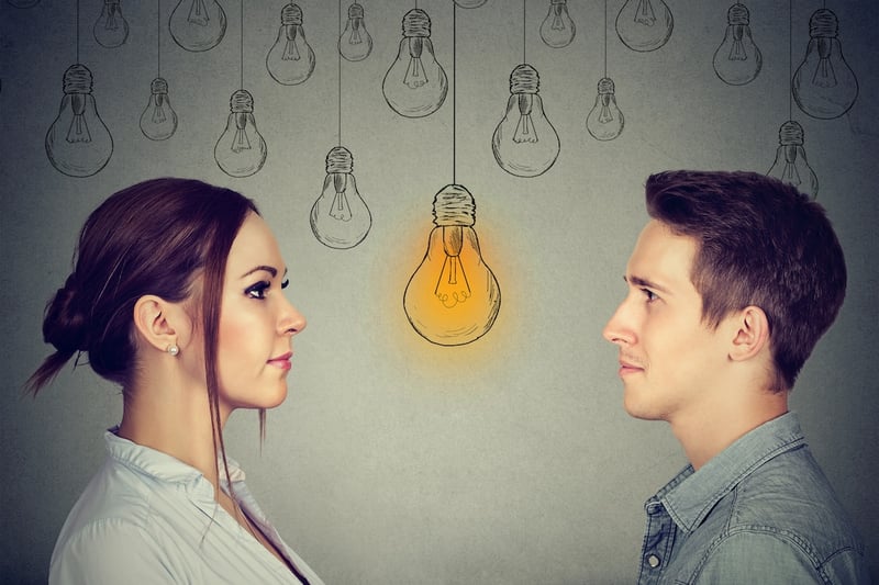 Men vs. Women Profile views of a young woman and a young man facing each other, set against a grey background adorned with hand-drawn lightbulbs. A single bright yellow lightbulb glows centrally between them, symbolizing the realization or "bright idea" regarding the shifting gender dynamics in higher education. This visual metaphor accompanies an analysis of the growing gender gap in college degree attainment, where women now outpace men in earning Associate's, Bachelor's, Master's, and Doctoral degrees. Source: The College Investor