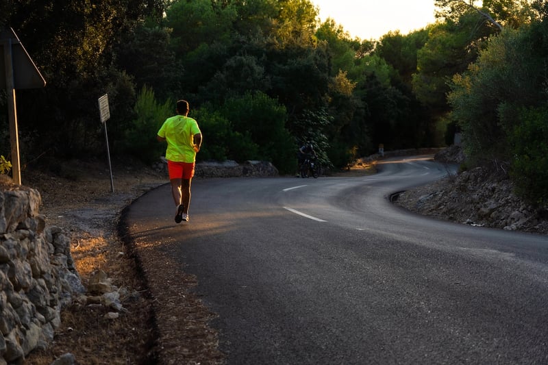 Young Spanish man running down a road in the middle of a pine forest with sunset in the background, man from behind wears striking sportswear Young man running down the road without limits, representing the upcoming graduate loan limits. Source: The College Investor
