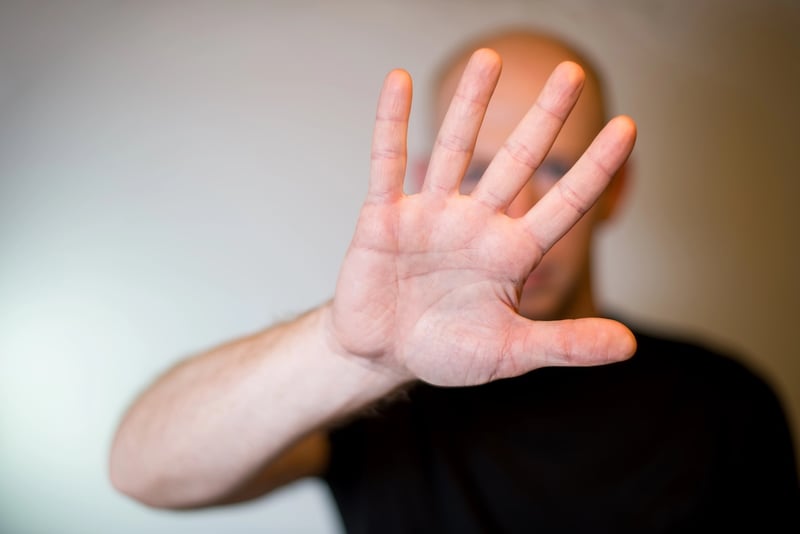 A person with a blurred face and bald head extends their right hand towards the viewer, palm open and fingers spread, in a clear "stop" or "hold" gesture. This image effectively symbolizes the Department of Education's decision to allow existing federal student loan borrowers to retain their current fixed repayment plans&mdash;Standard, Extended, and Graduated&mdash;after July 1, 2026. The hand gesture visually represents the pause or exemption for these borrowers from the new "tiered standard" repayment plan being introduced by the "One Big, Beautiful Bill Act" for future student loan recipients.