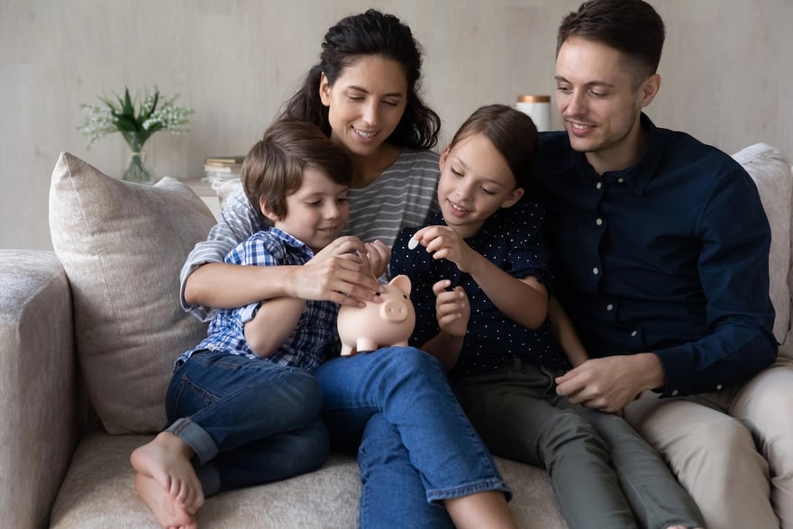 Happy couple parents teaching small children son daughter saving money. Caring young happy couple parents teaching small children son daughter saving money for future.