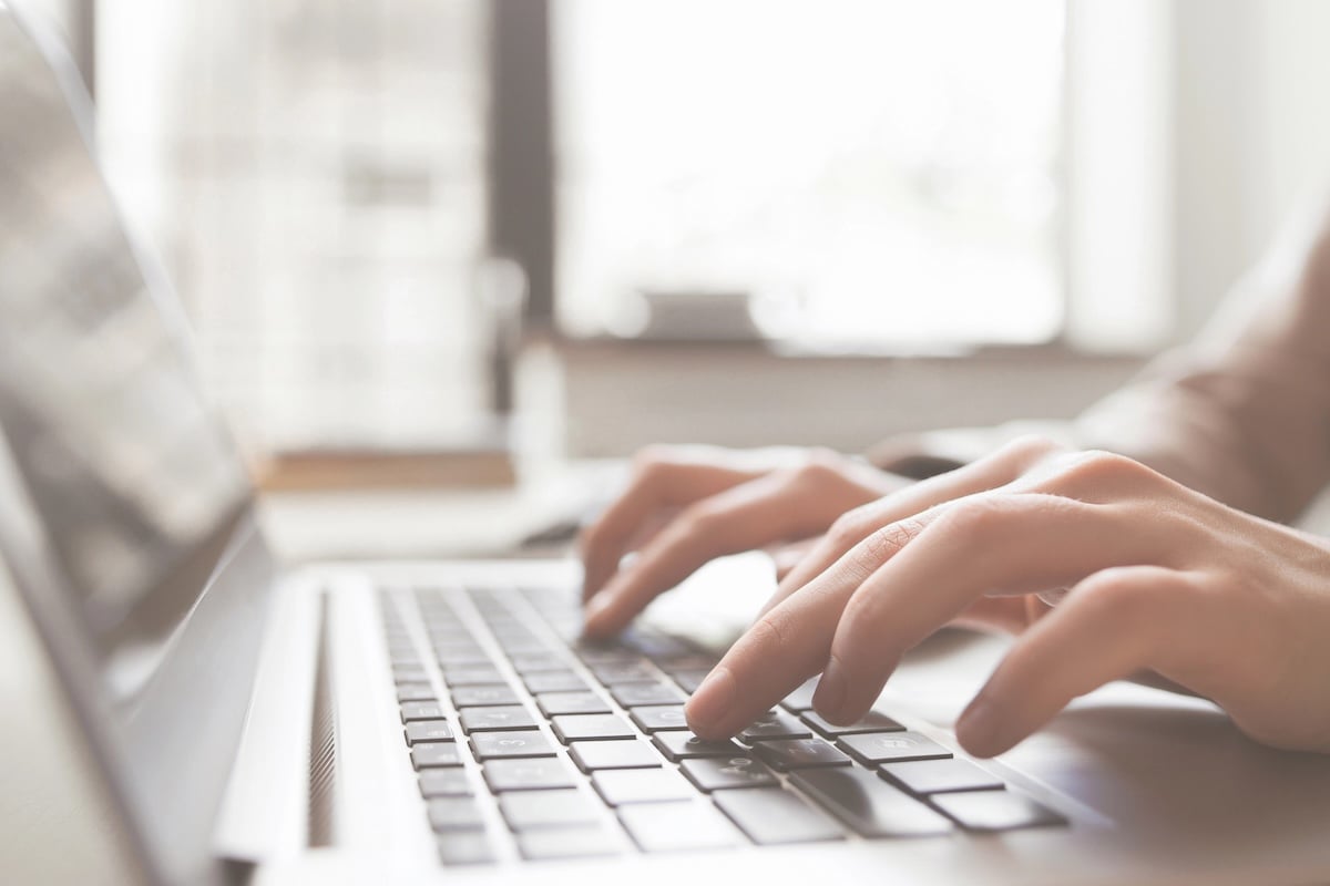 Close-up of a student&rsquo;s hands typing on a silver laptop keyboard next to textbooks and glasses. This image visualizes the urgency and focus required when applying for mid-year student loans or an Education Line of Credit to cover unexpected college expenses like housing or course fees after the semester has already begun. Source: The College Investor