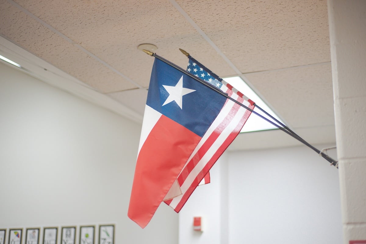 School in Dallas Fort Worth highlights Texas flag angled beside national banner on white wall.