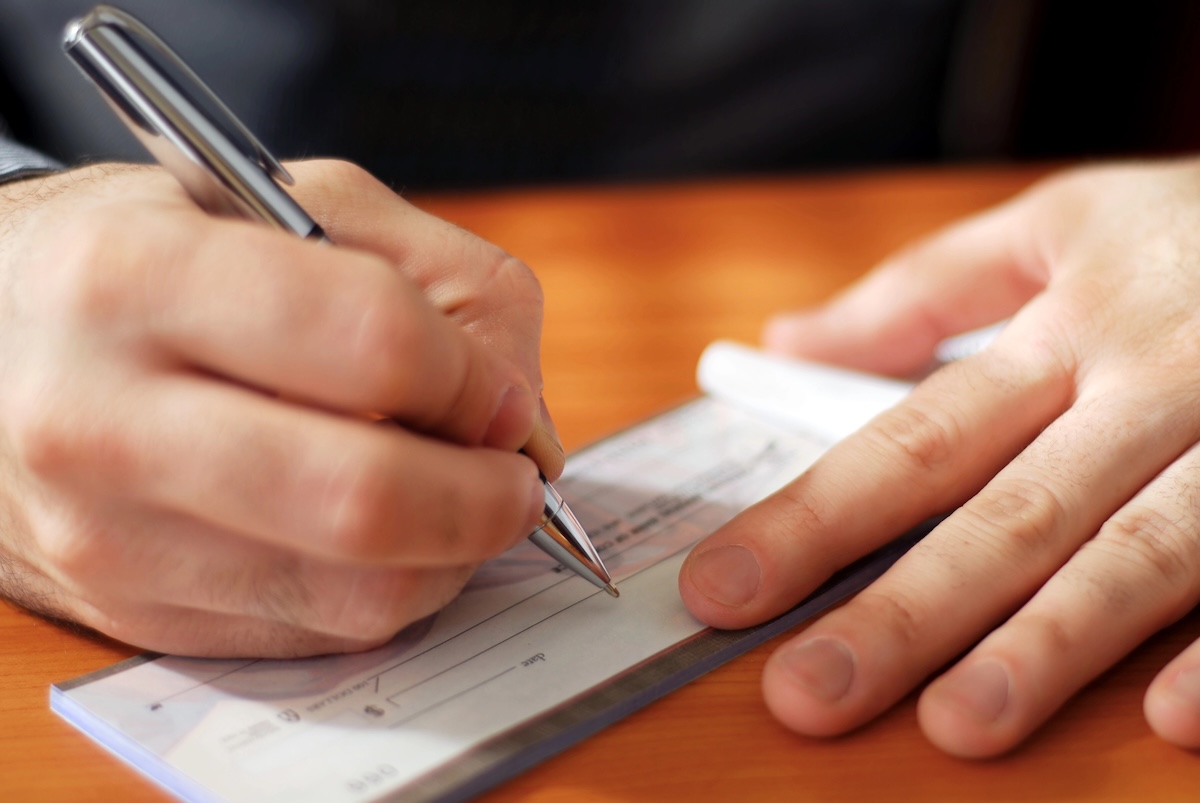 Man writing a check Closeup on man`s hands writing a check to pay off his student loans