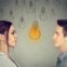Profile views of a young woman and a young man facing each other, set against a grey background adorned with hand-drawn lightbulbs. A single bright yellow lightbulb glows centrally between them, symbolizing the realization or "bright idea" regarding the shifting gender dynamics in higher education. This visual metaphor accompanies an analysis of the growing gender gap in college degree attainment, where women now outpace men in earning Associate's, Bachelor's, Master's, and Doctoral degrees. Source: The College Investor