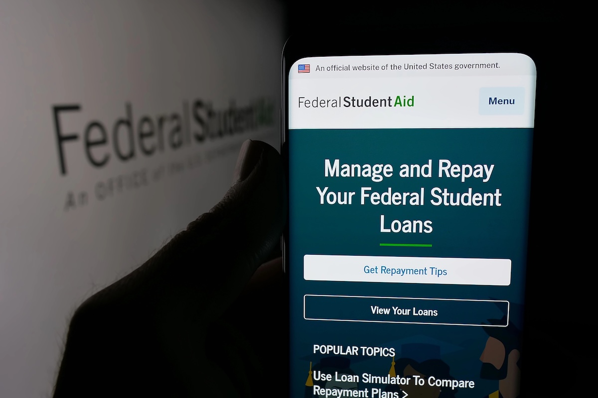 StudentAid Screenshot Phone Person holding smartphone with web page of education office Federal Student Aid (FSA) on screen in front of logo. Focus on center of phone display.